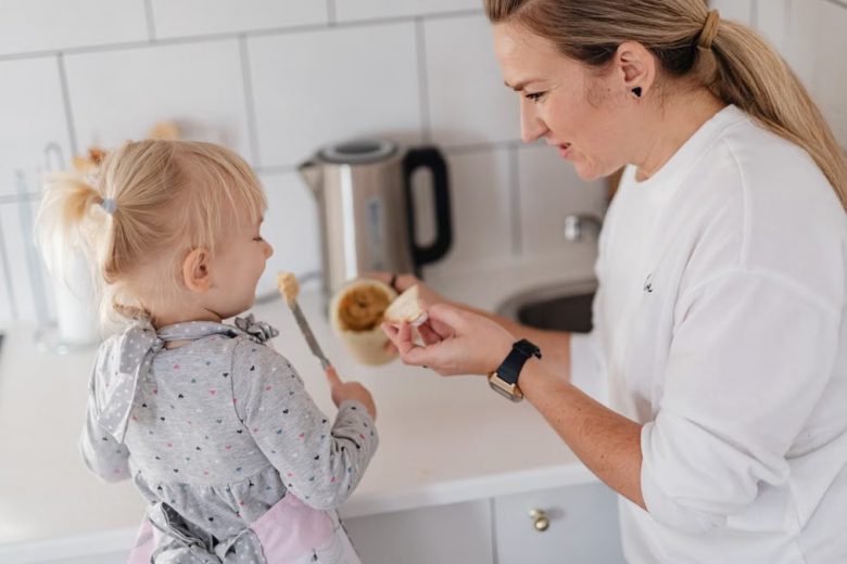 A mother and her young daughter interact while preparing food in a modern kitchen.